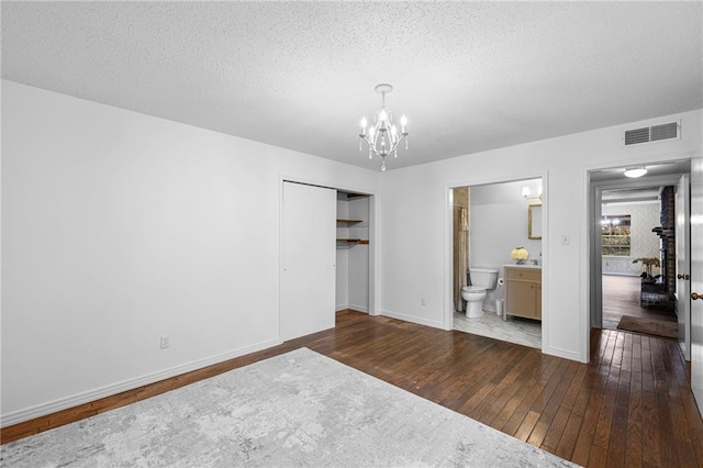 unfurnished bedroom featuring dark wood-style flooring, a closet, visible vents, a textured ceiling, and a chandelier