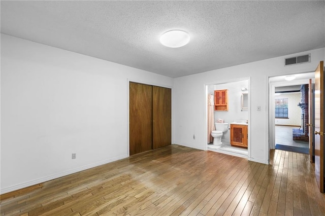 unfurnished bedroom featuring a closet, connected bathroom, a textured ceiling, and hardwood / wood-style floors