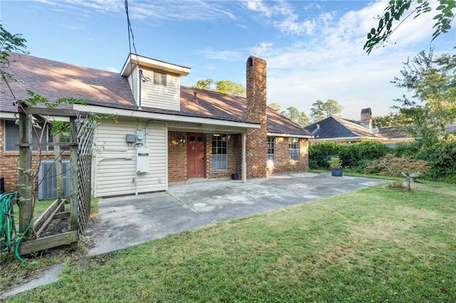 back of property featuring a patio, brick siding, a lawn, and a chimney