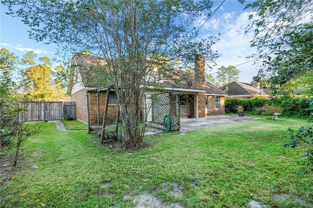 rear view of property featuring a fenced backyard, brick siding, a lawn, a chimney, and a patio area