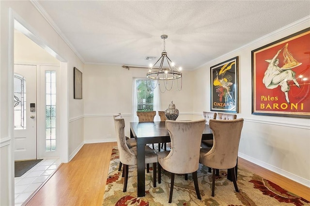 dining room with crown molding, a notable chandelier, a textured ceiling, and light wood-type flooring