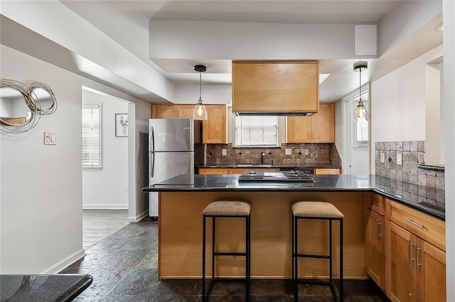 kitchen with kitchen peninsula, stainless steel fridge, tasteful backsplash, hanging light fixtures, and a kitchen breakfast bar