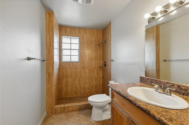 bathroom with vanity, a tile shower, toilet, and tile patterned flooring