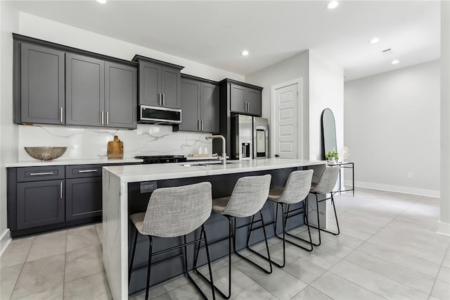 kitchen with decorative backsplash, a kitchen breakfast bar, stainless steel appliances, a center island with sink, and sink