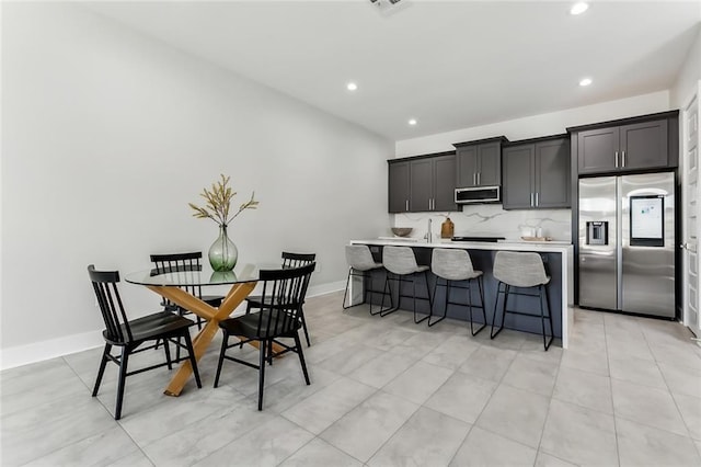 kitchen featuring backsplash, a kitchen island with sink, a kitchen bar, sink, and stainless steel appliances