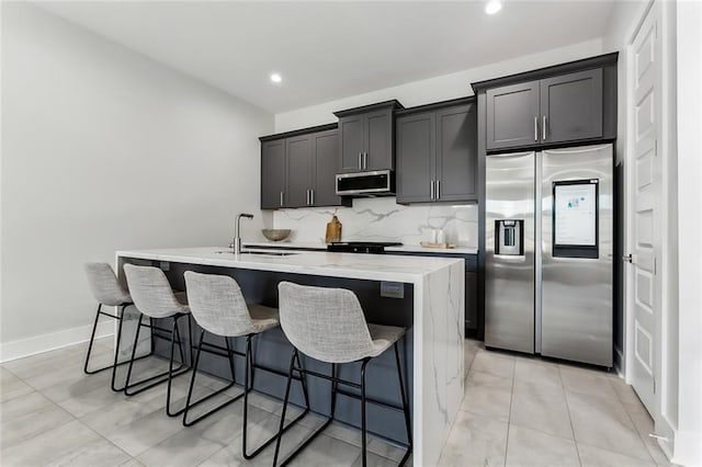 kitchen with tasteful backsplash, appliances with stainless steel finishes, sink, a breakfast bar area, and a center island with sink