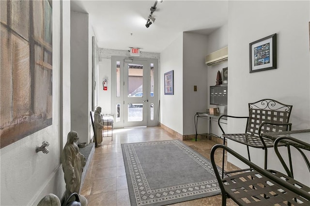 hall with light tile patterned floors, a wealth of natural light, a wall unit AC, and rail lighting