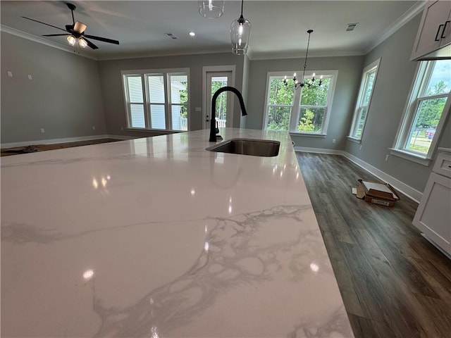 kitchen with hanging light fixtures, light stone counters, dark wood-style flooring, a sink, and crown molding