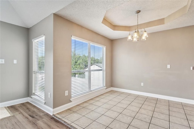 unfurnished dining area featuring a notable chandelier, a textured ceiling, light hardwood / wood-style flooring, and a raised ceiling