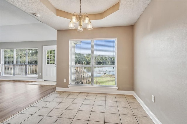 unfurnished dining area featuring an inviting chandelier, light hardwood / wood-style flooring, a textured ceiling, and a tray ceiling