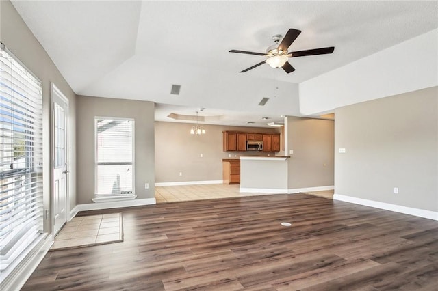 unfurnished living room with a wealth of natural light, lofted ceiling, ceiling fan with notable chandelier, and dark hardwood / wood-style flooring