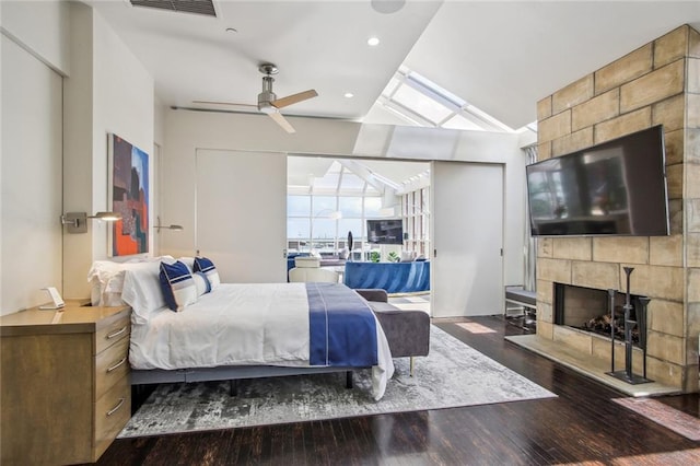 bedroom featuring dark wood-type flooring, vaulted ceiling with skylight, a tile fireplace, and ceiling fan