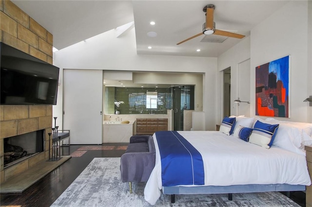 bedroom featuring dark wood-type flooring, ceiling fan, ensuite bathroom, and a tile fireplace