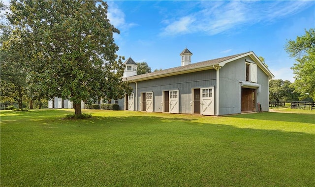 rear view of property featuring a lawn, a barn, fence, and an outbuilding