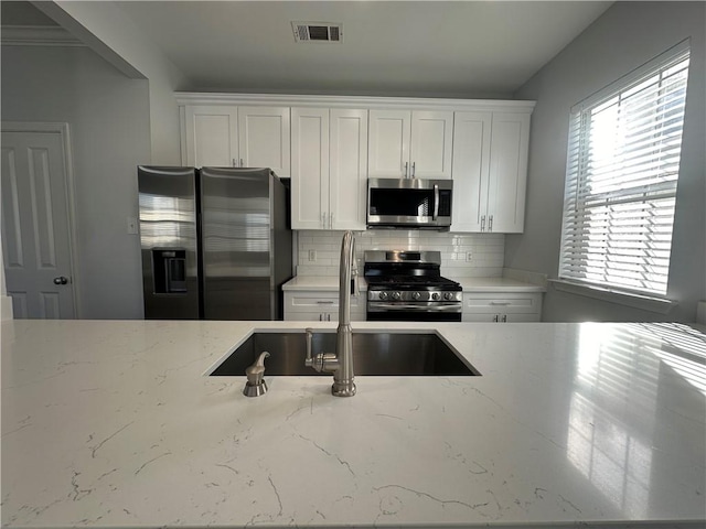 kitchen featuring white cabinetry, light stone countertops, appliances with stainless steel finishes, and decorative backsplash