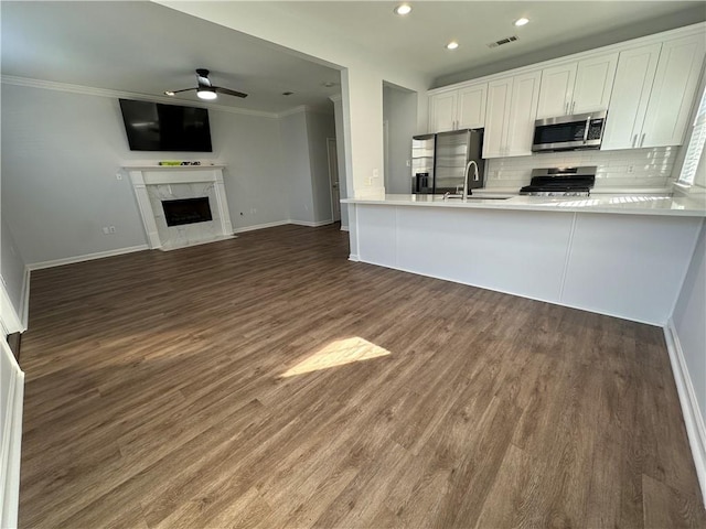 kitchen featuring dark wood-type flooring, kitchen peninsula, crown molding, white cabinets, and appliances with stainless steel finishes