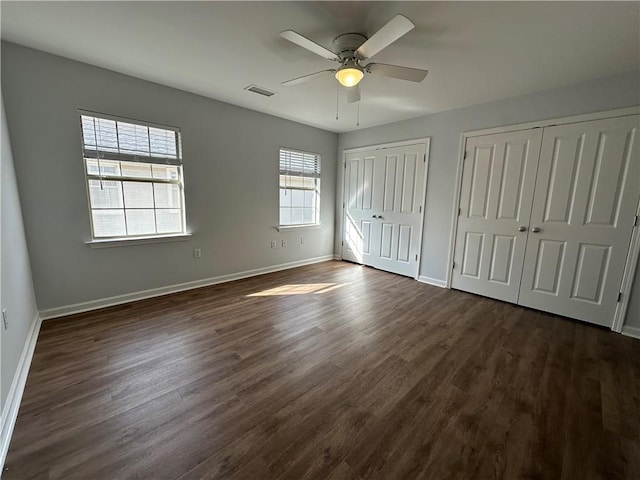 unfurnished bedroom with dark wood-type flooring, ceiling fan, and multiple closets