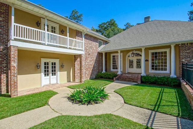 view of exterior entry with stucco siding, a balcony, french doors, and brick siding