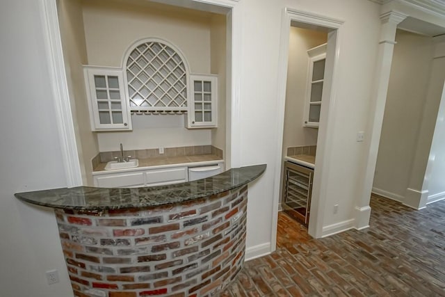 bar with white cabinets, dishwasher, sink, ornate columns, and beverage cooler