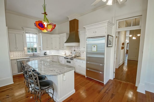 kitchen featuring wall chimney exhaust hood, high quality appliances, sink, white cabinets, and tasteful backsplash