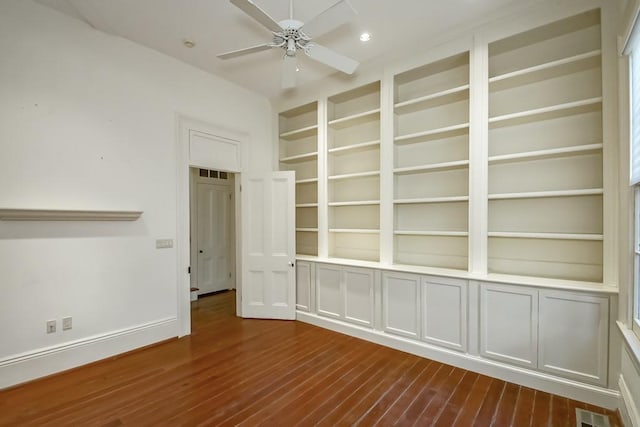 unfurnished room featuring dark wood-type flooring, built in shelves, and ceiling fan