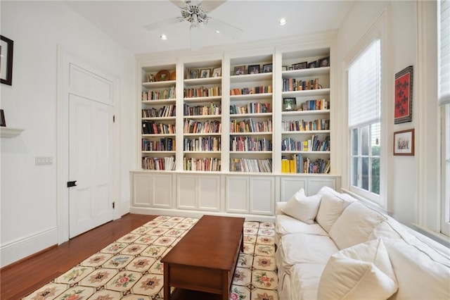 living area with dark wood-type flooring, ceiling fan, and built in shelves