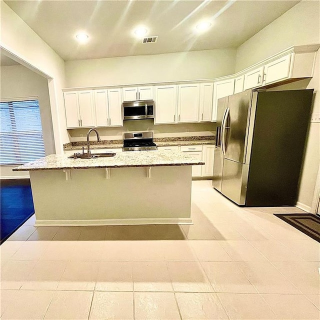 kitchen featuring sink, appliances with stainless steel finishes, light stone counters, and a kitchen island with sink