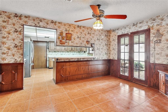 kitchen with french doors, a textured ceiling, stainless steel refrigerator, and wooden walls