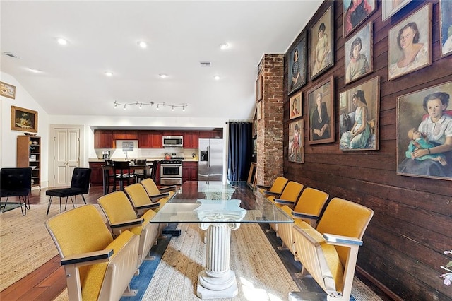 dining area featuring rail lighting, wood-type flooring, and vaulted ceiling