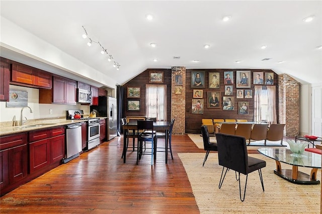 kitchen with lofted ceiling, light stone counters, stainless steel appliances, dark wood-type flooring, and sink