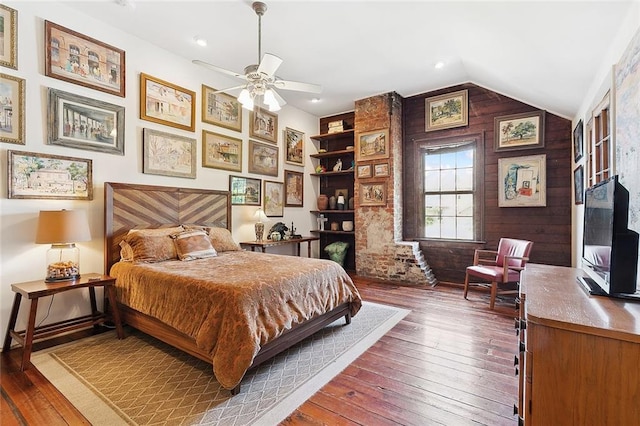 bedroom featuring dark hardwood / wood-style flooring, lofted ceiling, wood walls, and ceiling fan