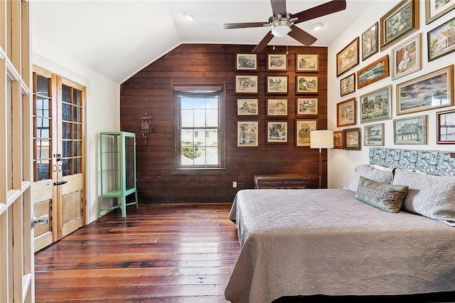 bedroom featuring dark hardwood / wood-style flooring, wooden walls, vaulted ceiling, and ceiling fan