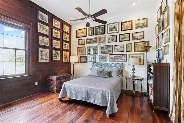 bedroom featuring wood walls, dark wood-type flooring, vaulted ceiling, and ceiling fan