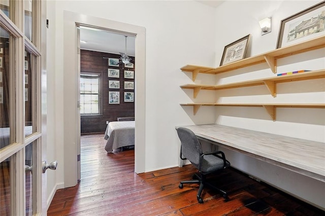 office area featuring dark hardwood / wood-style flooring, ceiling fan, built in desk, and wooden walls