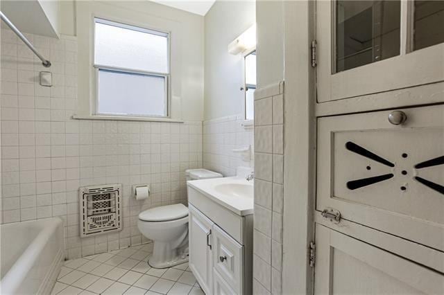 full bathroom with heating unit, tile walls, toilet, vanity, and tile patterned floors