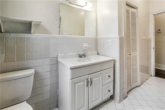 bathroom with toilet, vanity, tile patterned floors, and tile walls