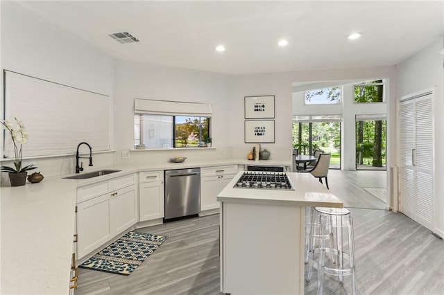 kitchen with stainless steel appliances, white cabinets, sink, a kitchen breakfast bar, and light wood-type flooring