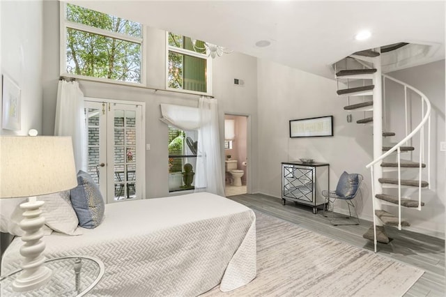 bedroom with a high ceiling, access to outside, multiple windows, and hardwood / wood-style flooring