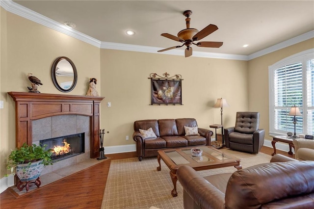 living room with ceiling fan, a tiled fireplace, crown molding, and hardwood / wood-style floors