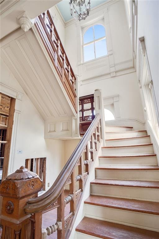 stairs featuring a towering ceiling, an inviting chandelier, and crown molding