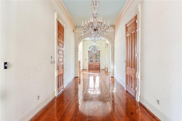 hallway with wood-type flooring, ornamental molding, and an inviting chandelier