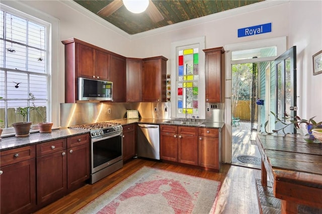 kitchen featuring stainless steel appliances, a sink, dark stone countertops, plenty of natural light, and dark wood finished floors