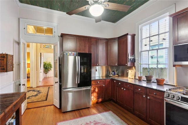 kitchen featuring stainless steel appliances, dark stone counters, a wealth of natural light, and wood finished floors