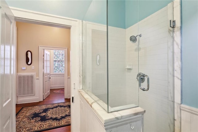 bathroom with wood finished floors, a shower stall, and visible vents