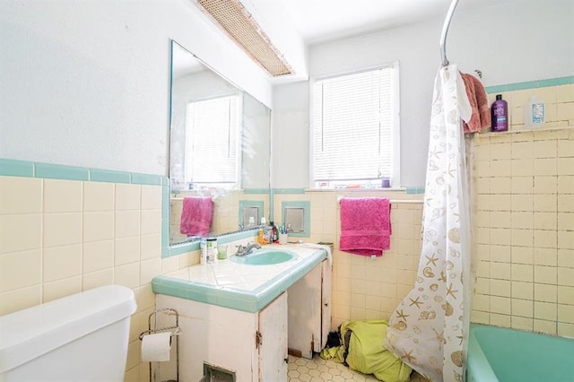 full bathroom with a healthy amount of sunlight, vanity, toilet, and tile walls