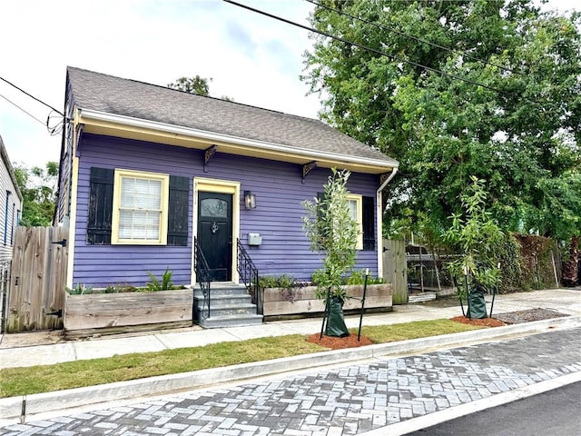 view of front of property with entry steps, a shingled roof, and fence