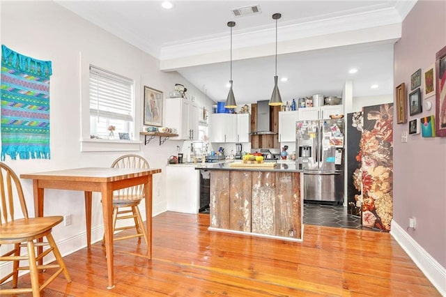 kitchen with visible vents, wall chimney range hood, stainless steel fridge with ice dispenser, light wood-style floors, and white cabinetry