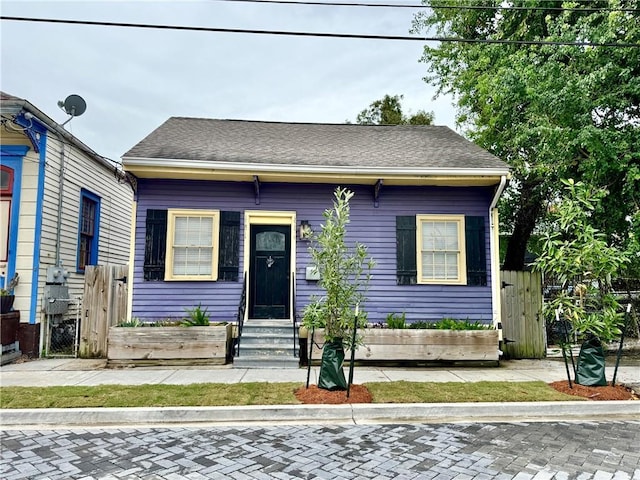 view of front facade with fence, roof with shingles, and a gate