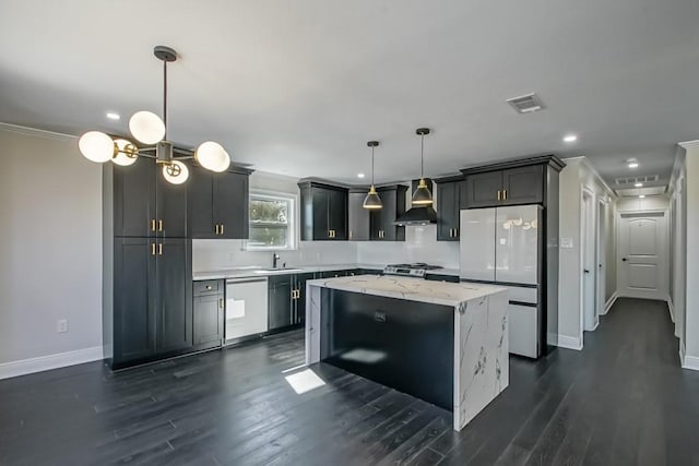 kitchen with appliances with stainless steel finishes, sink, a kitchen island, wall chimney exhaust hood, and decorative light fixtures