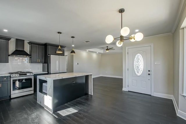 kitchen featuring a kitchen island, wall chimney range hood, decorative light fixtures, appliances with stainless steel finishes, and ceiling fan with notable chandelier